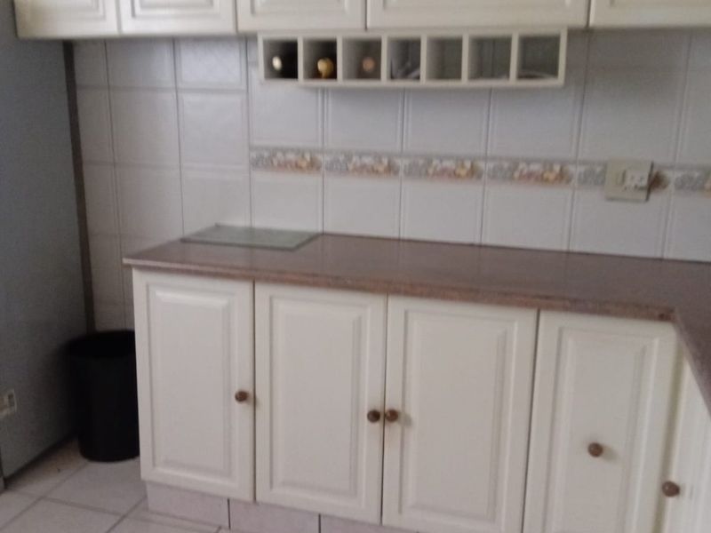 A functional kitchen area featuring white built-in cabinetry, tiled backsplash, and ceramic floor tiles, offering a clean and practical workspace.