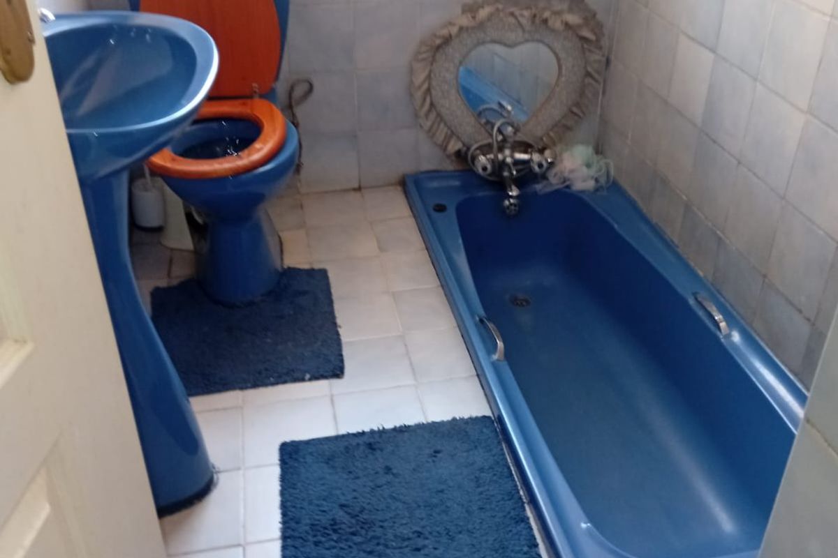 A dated bathroom featuring blue sanitaryware, including a pedestal basin, toilet, and built-in bathtub, with full-height wall tiling and floor tiles.