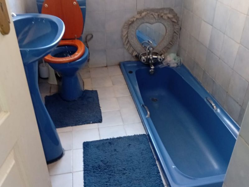 A dated bathroom featuring blue sanitaryware, including a pedestal basin, toilet, and built-in bathtub, with full-height wall tiling and floor tiles.