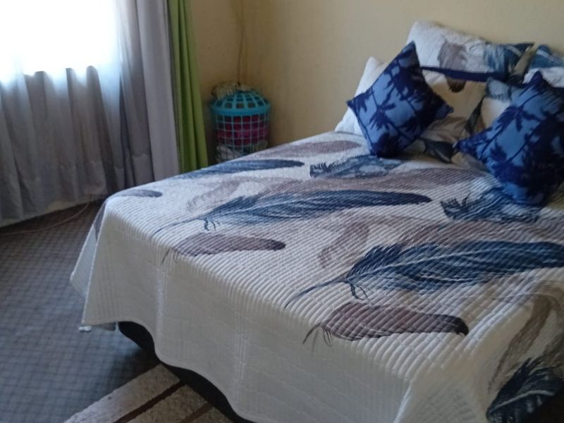 A bedroom featuring carpeted flooring and a window with curtains. The room shows signs of wear on the walls and requires minor cosmetic updates.