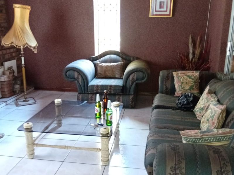 A living room featuring tiled flooring and a timber ceiling, with a narrow window fitted with security bars.