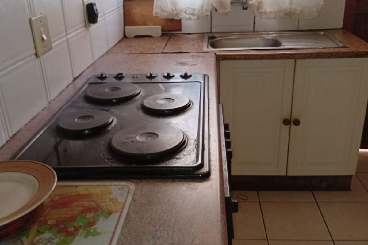 A functional kitchen featuring a built-in electric hob, extractor fan, stainless steel sink, and tiled splashback with laminate countertops and cabinetry.