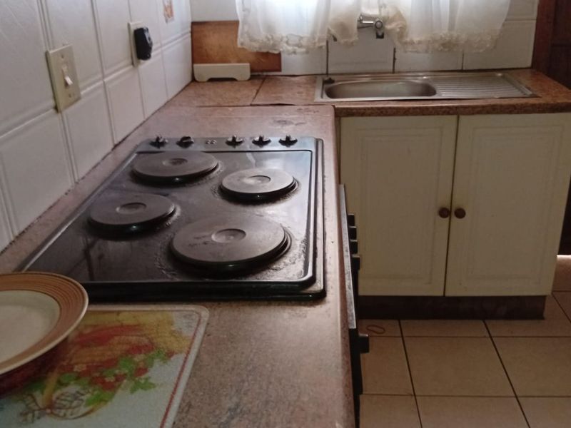 A functional kitchen featuring a built-in electric hob, extractor fan, stainless steel sink, and tiled splashback with laminate countertops and cabinetry.
