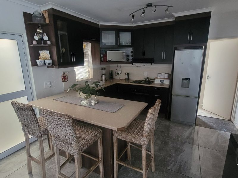 A functional kitchen featuring dark cabinetry, stone countertops, a breakfast bar, and tiled flooring, providing a practical layout for cooking and dining.