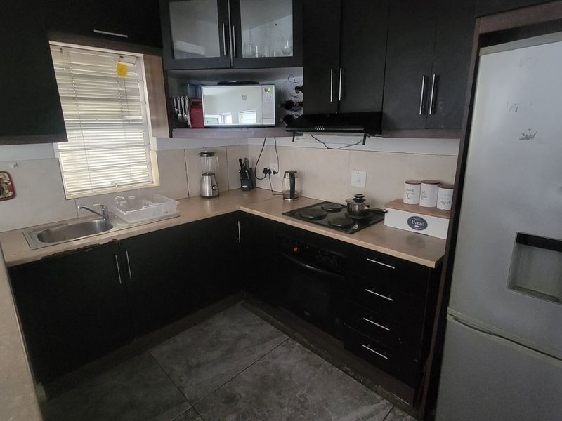 Functional kitchen featuring dark cabinetry, laminate countertops, integrated electric hob and oven, extractor fan, and tiled flooring.