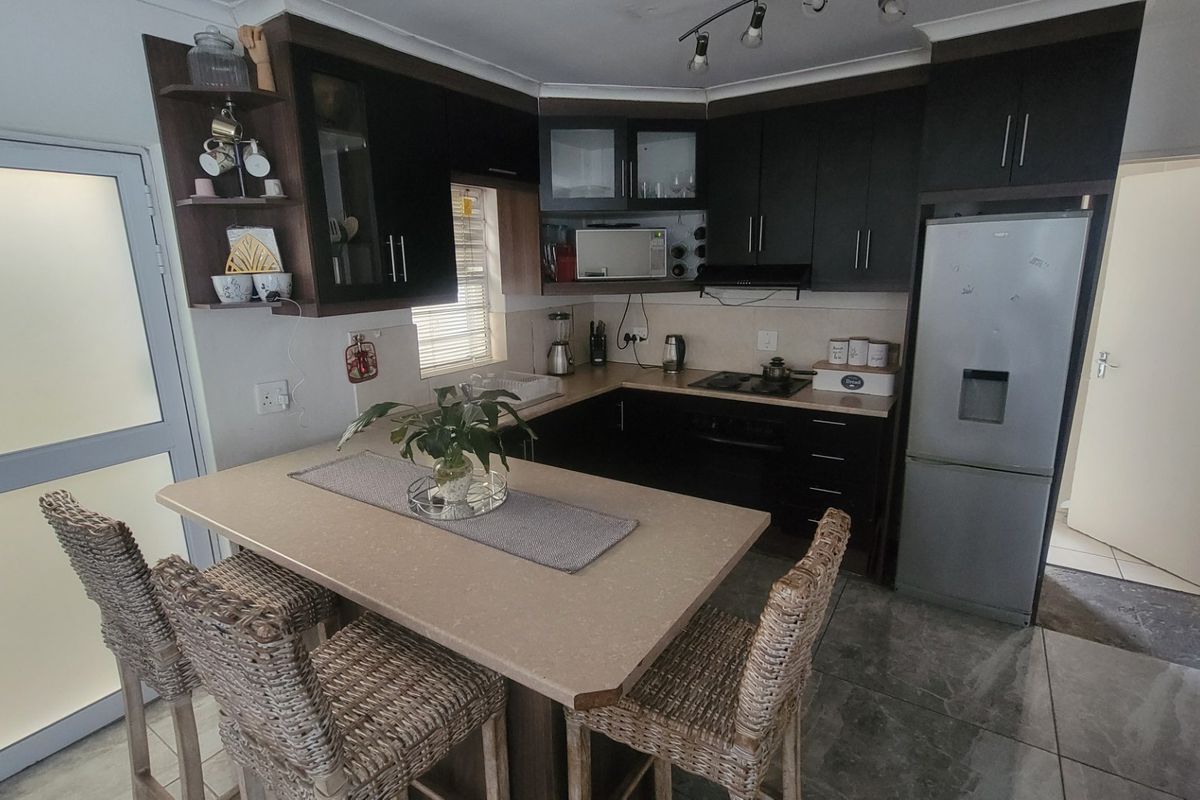 A functional kitchen featuring dark cabinetry, a stone-look breakfast bar, built-in appliances, and tiled flooring, offering a practical layout for daily use.