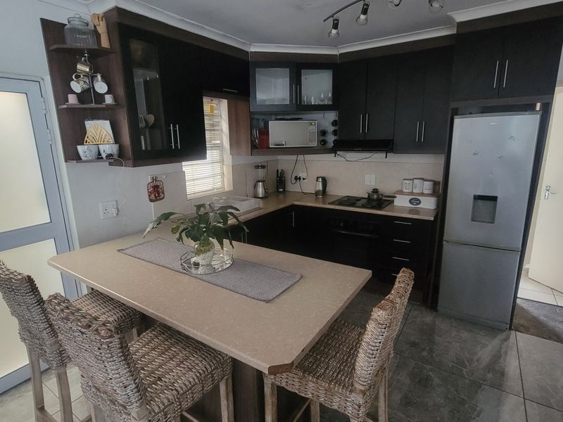 A functional kitchen featuring dark cabinetry, a stone-look breakfast bar, built-in appliances, and tiled flooring, offering a practical layout for daily use.