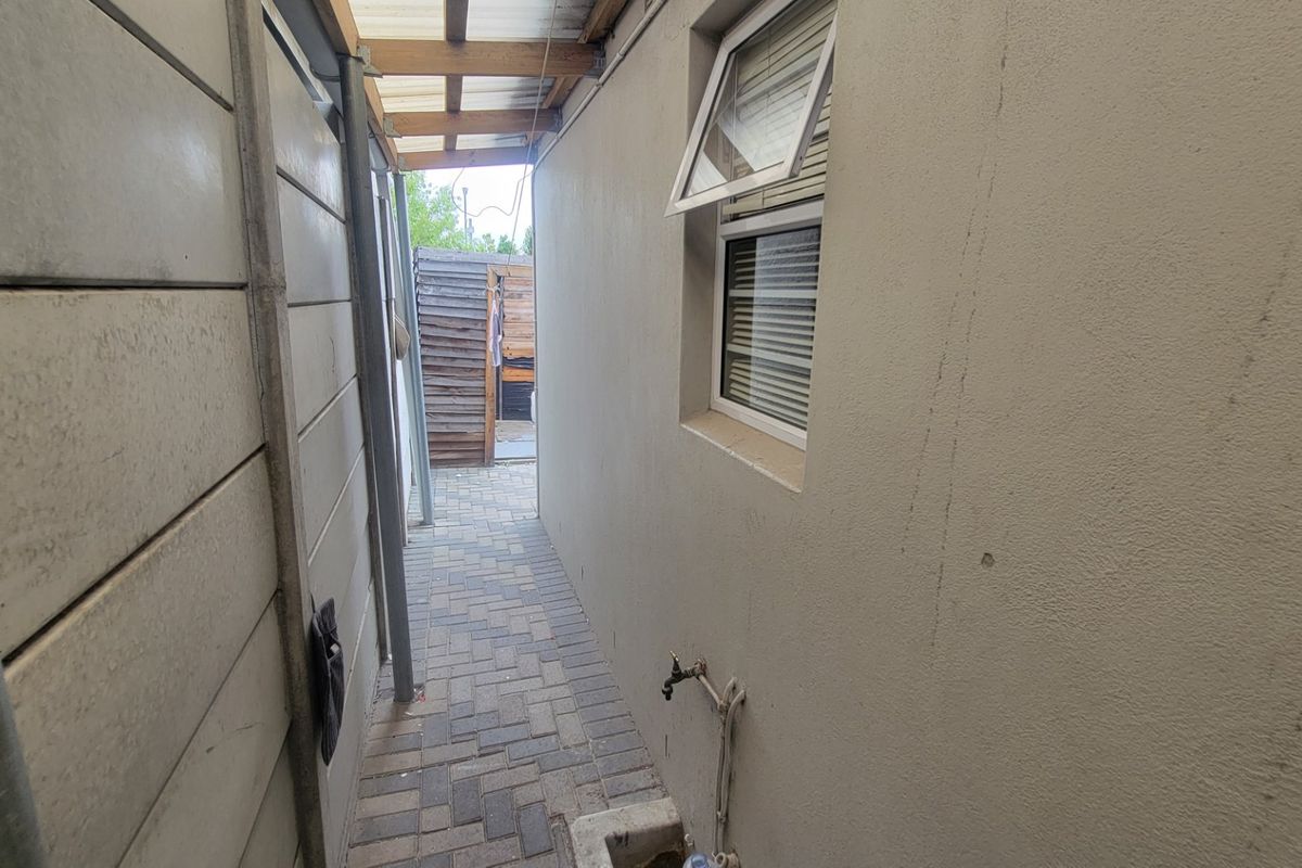 A narrow side passage featuring paved flooring, a precast concrete boundary wall, and an external water tap.