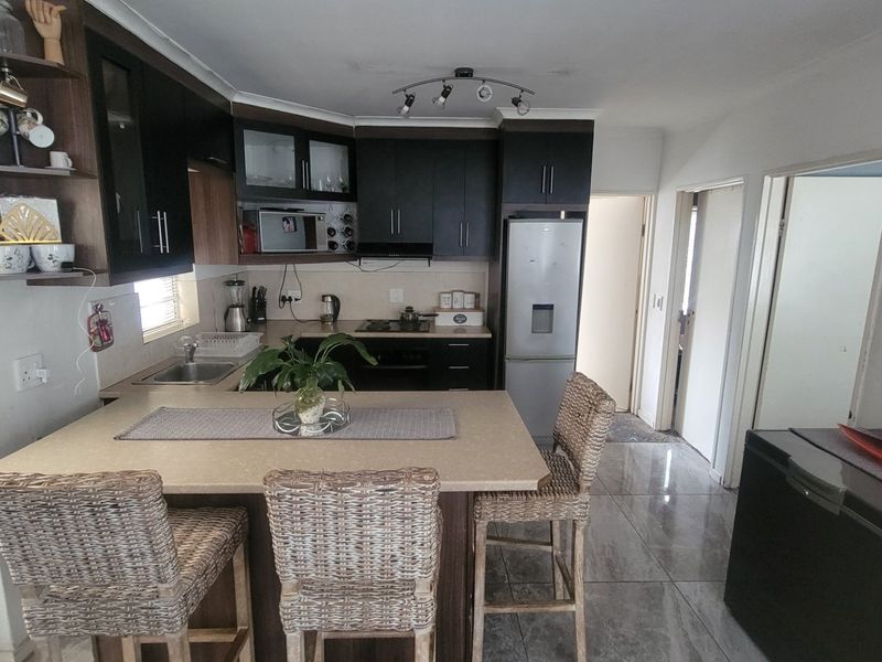 A functional kitchen featuring dark cabinetry, stone countertops, a breakfast bar, and integrated appliances, complemented by modern tiled flooring.
