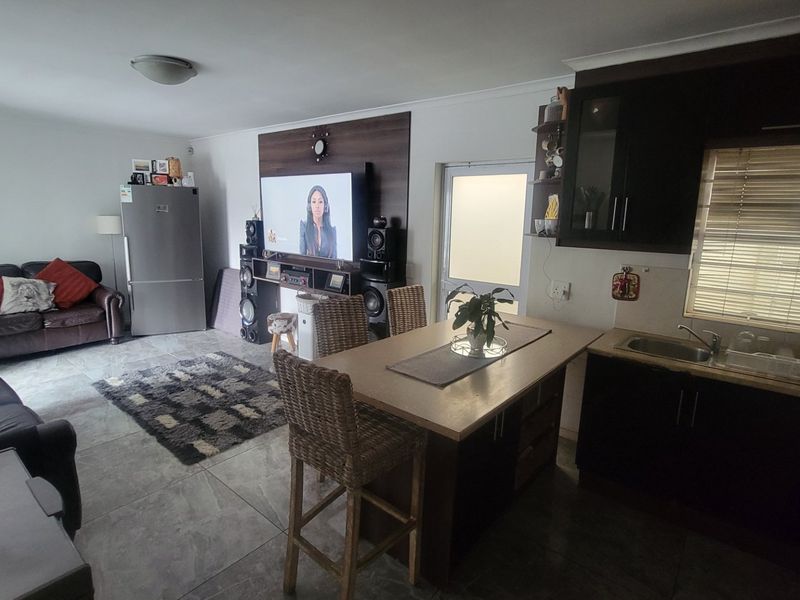 Open-plan living area featuring a kitchen with dark cabinetry, tiled flooring, and a dedicated media wall, creating a functional and connected living space.