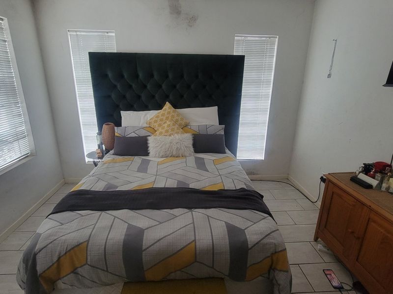 A bedroom featuring tiled flooring and dual windows with venetian blinds, showing visible signs of ceiling water damage and wall wear.
