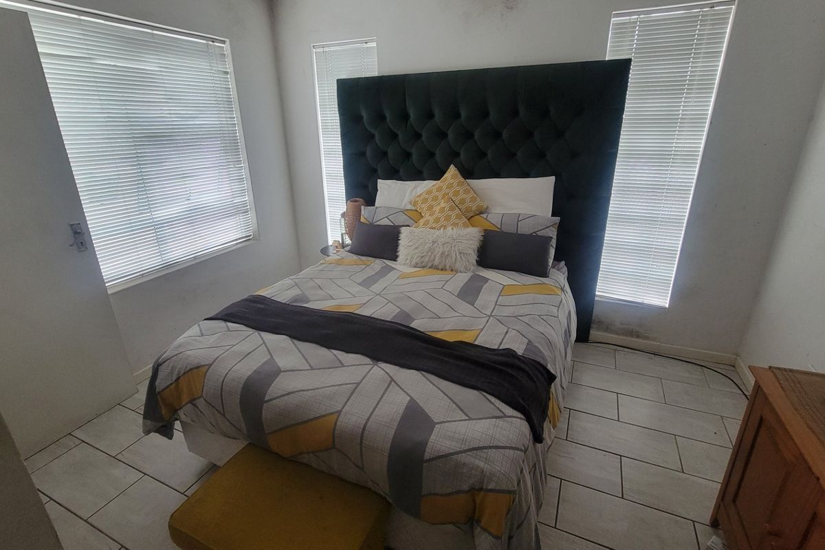 A bedroom featuring tiled flooring and venetian blinds, showing signs of wall dampness near the window area.