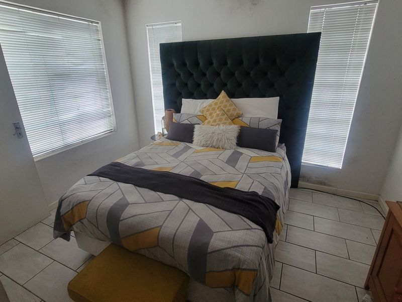 A bedroom featuring tiled flooring and venetian blinds, showing signs of wall dampness near the window area.