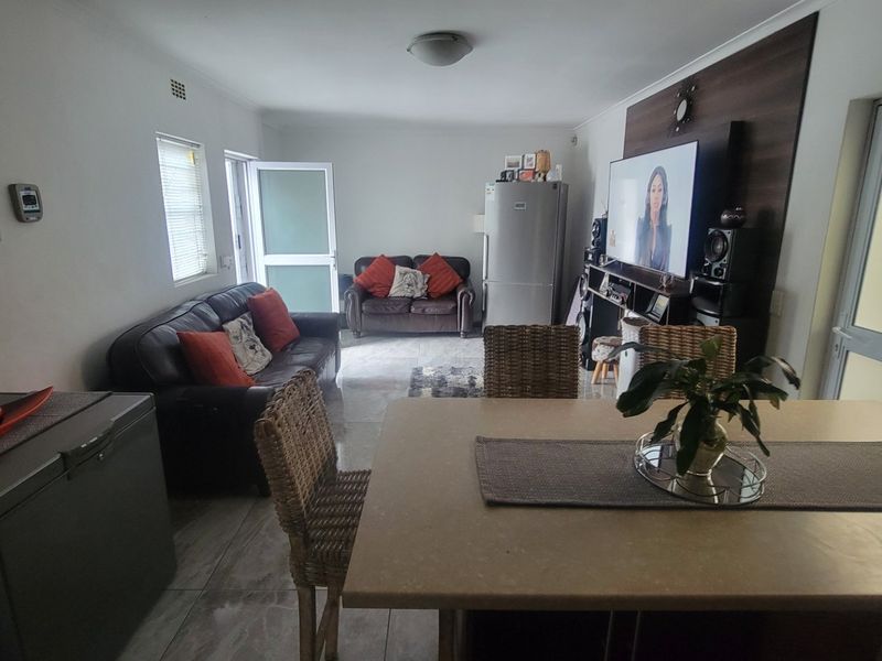 Open-plan living and dining area featuring tiled flooring, a decorative feature wall, and direct access to the exterior via a sliding glass door.