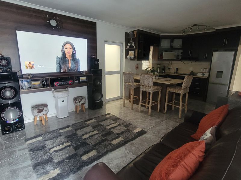 Open-plan living and kitchen area featuring tiled flooring, a built-in media wall, and dark wood cabinetry with a central kitchen island.
