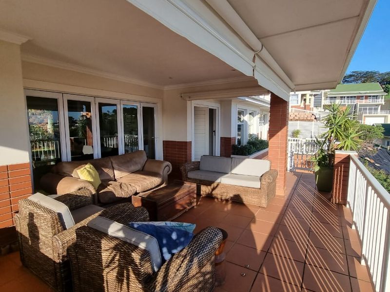 Spacious covered balcony featuring tiled flooring, brick accents, and a white metal balustrade, offering a comfortable outdoor living space with sliding door access.