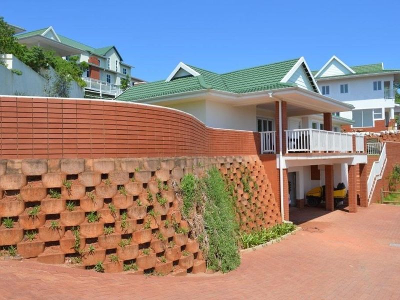 Front exterior view of a townhouse featuring a prominent brick retaining wall, paved driveway, and a balcony with white railings.