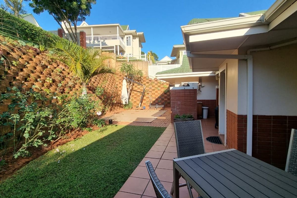 A private rear garden featuring a paved patio area, a well-maintained lawn, and a tiered retaining wall with established landscaping.