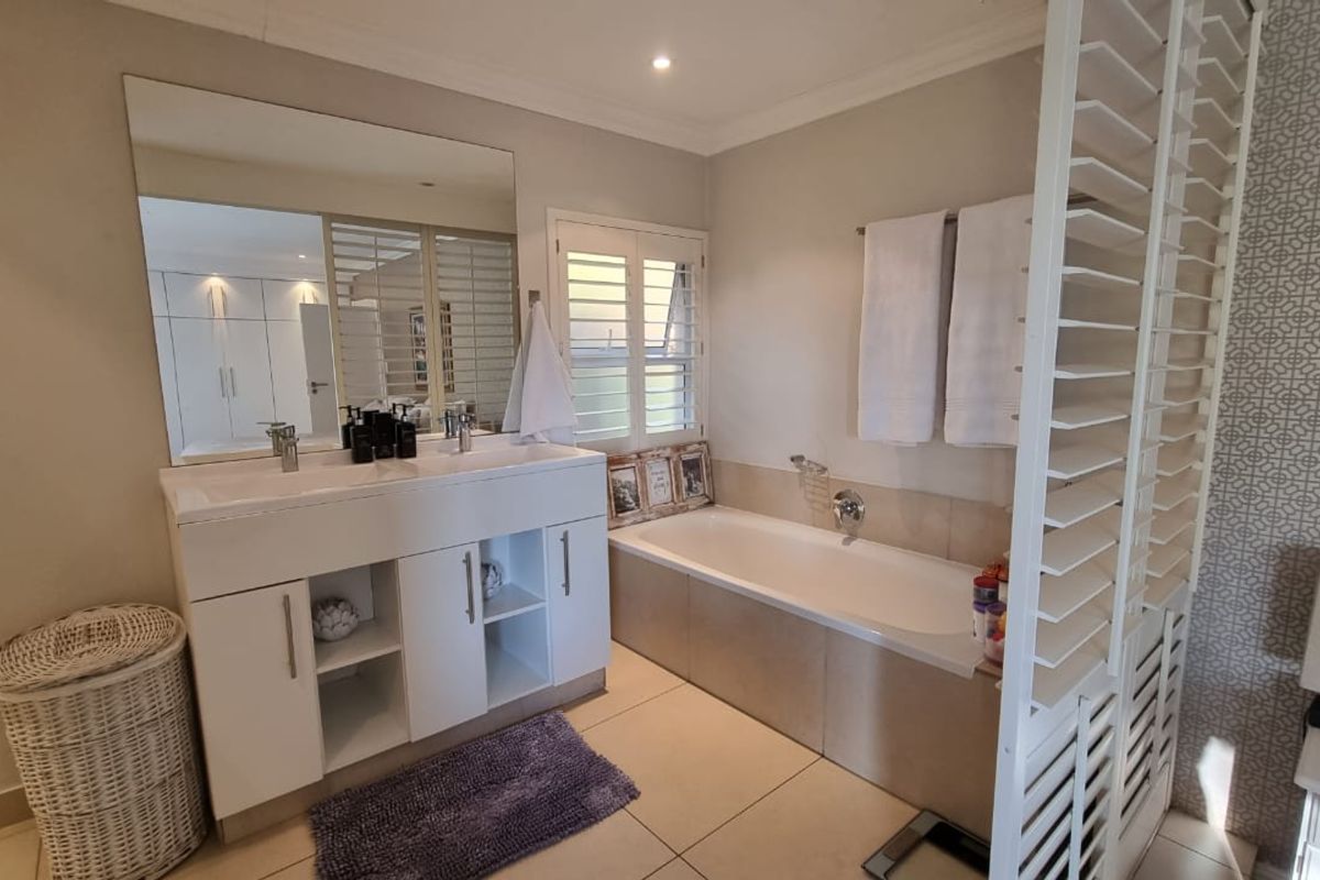 A well-maintained bathroom featuring a double vanity, a built-in bathtub, and plantation shutters, offering a clean and functional space.