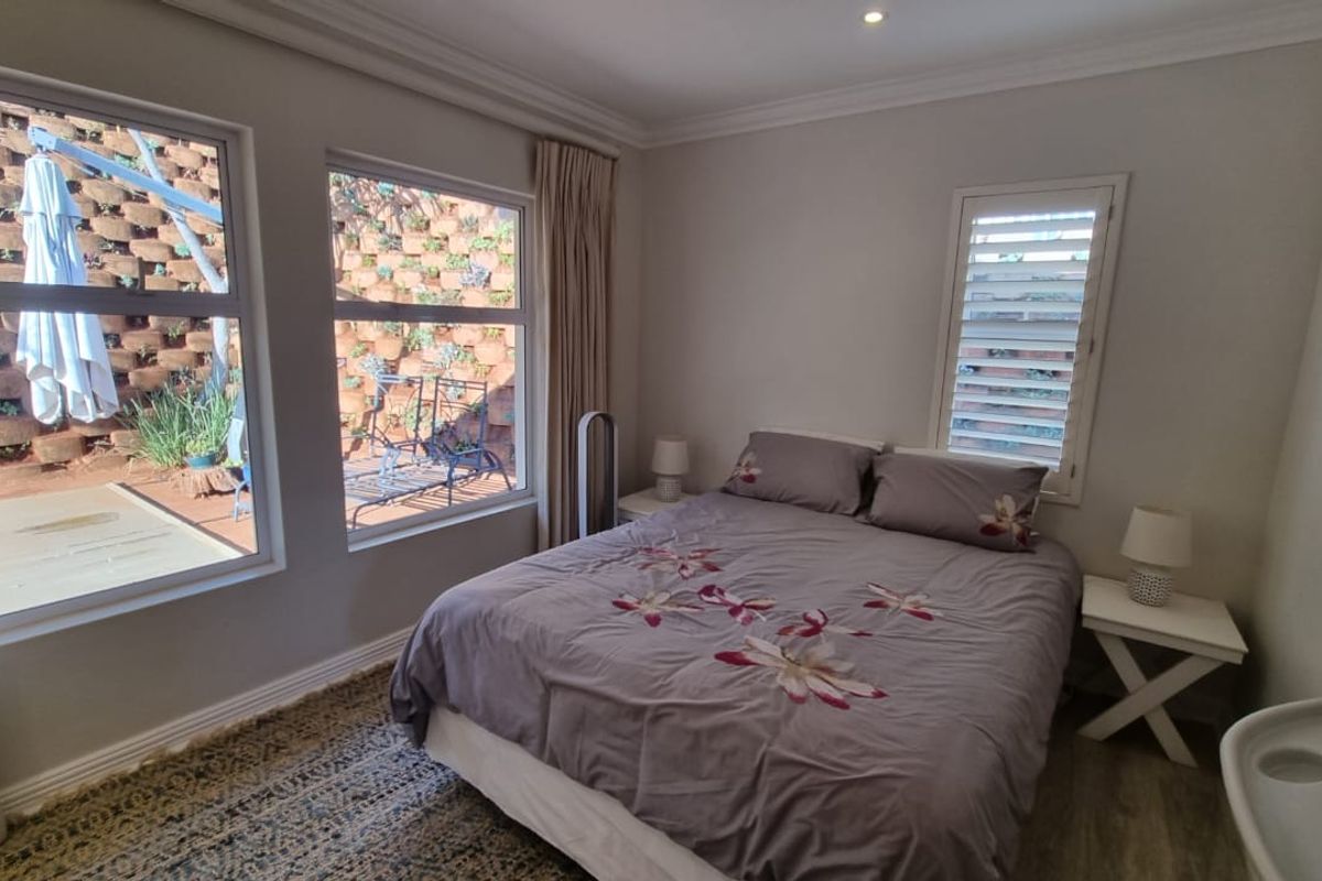 A well-lit bedroom featuring laminate flooring, plantation shutters, and recessed downlighting, offering a pleasant view of the terraced garden area.