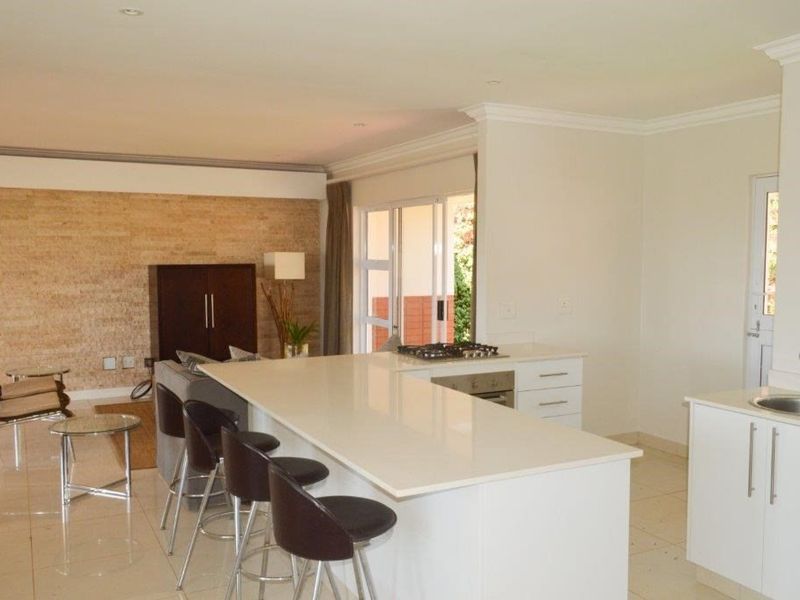 Spacious open-plan living area featuring a modern kitchen with a large island, stone countertop, built-in appliances, and a striking stone feature wall.