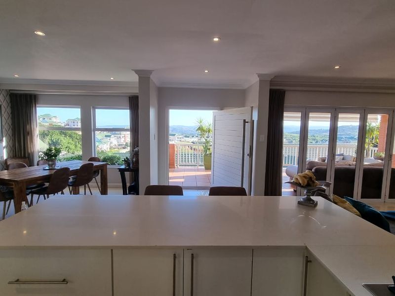Spacious open-plan living and dining area featuring a modern kitchen island, recessed lighting, and large bi-fold doors opening to a scenic outdoor balcony.