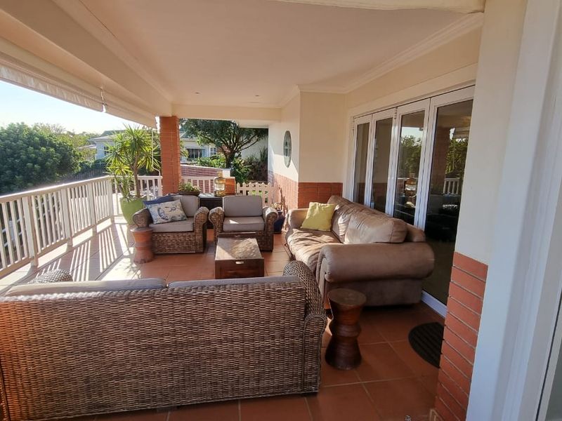 A spacious covered patio featuring tiled flooring, brick pillars, and white balustrades, providing a comfortable outdoor living area with access through folding glass doors.