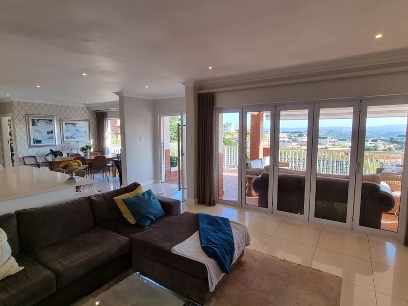 Spacious open-plan living and dining area featuring tiled floors, recessed lighting, and large folding glass doors opening onto a patio with scenic views.