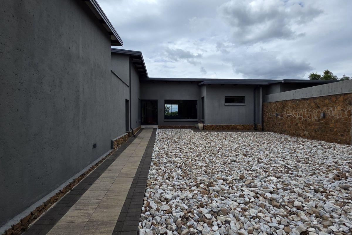 A modern rear exterior view featuring grey rendered walls, stone cladding accents, a paved walkway, and a low-maintenance gravel courtyard area.