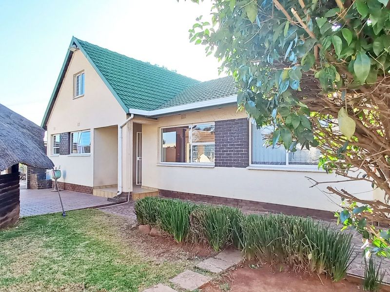 Rear view of the property featuring a paved patio area, a traditional thatched lapa, and a well-maintained garden with established landscaping.
