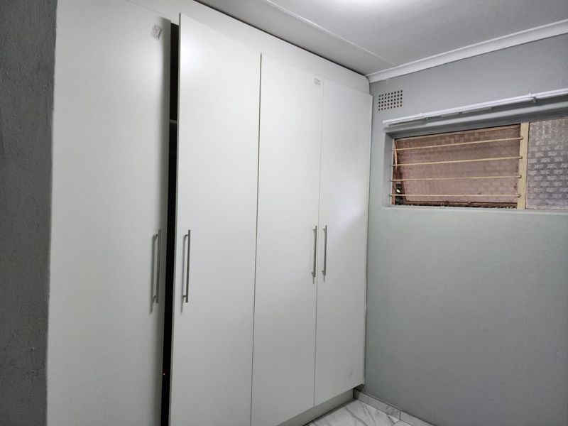 A bedroom featuring built-in cupboards, tiled flooring, and a top-hung window with security bars.