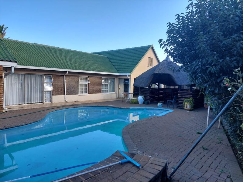 Outdoor pool area featuring a swimming pool, brick paving, and a thatched lapa, set against the rear elevation of the property.