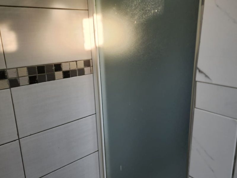 A close-up view of a shower enclosure featuring frosted glass doors, ceramic wall tiling with a decorative mosaic border, and tiled flooring.