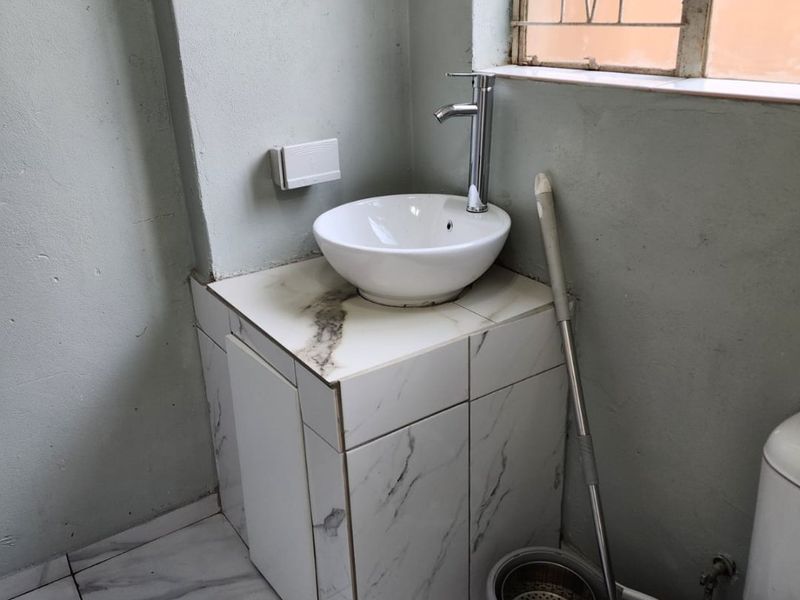 A small bathroom featuring a vessel sink on a tiled vanity, marble-look floor tiles, and a toilet, requiring minor finishing touches to improve aesthetics.