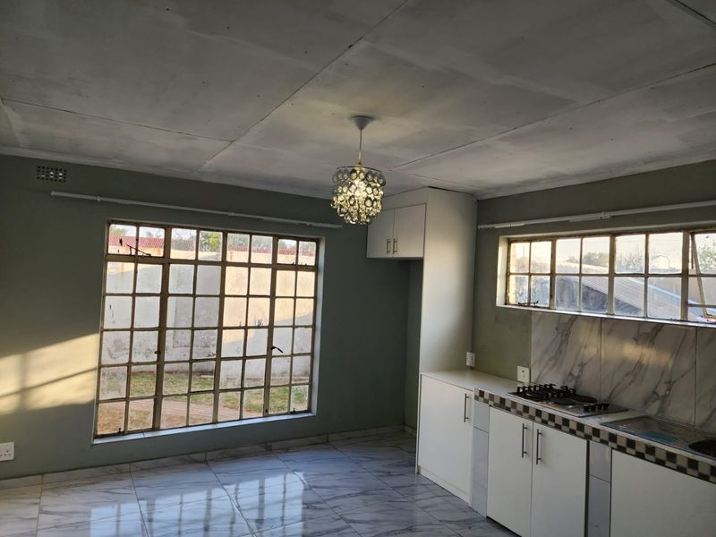 Open-plan kitchen and living area featuring marble-look floor tiles, built-in cabinetry with gas hob, and large steel-framed windows providing natural light.