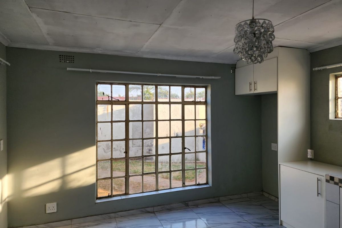 An empty kitchen area featuring tiled flooring, built-in cabinetry, and a large steel-framed window providing natural light.