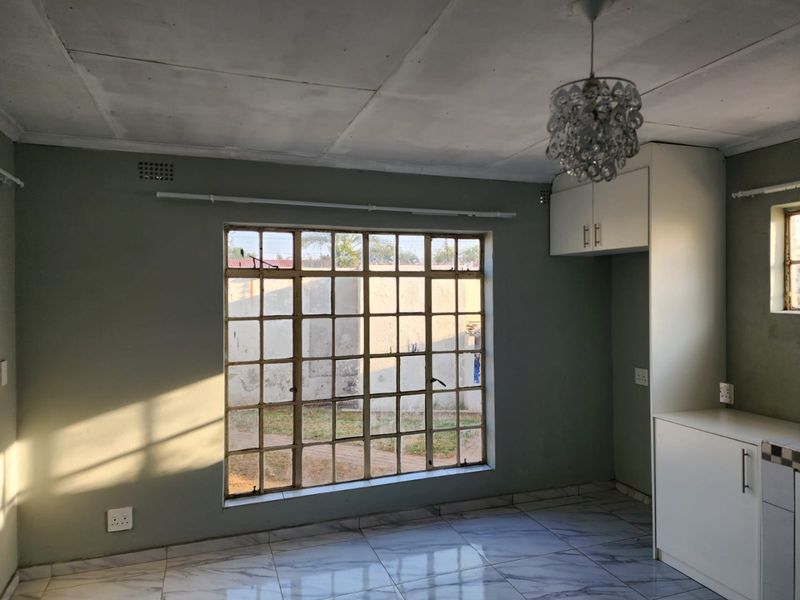An empty kitchen area featuring tiled flooring, built-in cabinetry, and a large steel-framed window providing natural light.