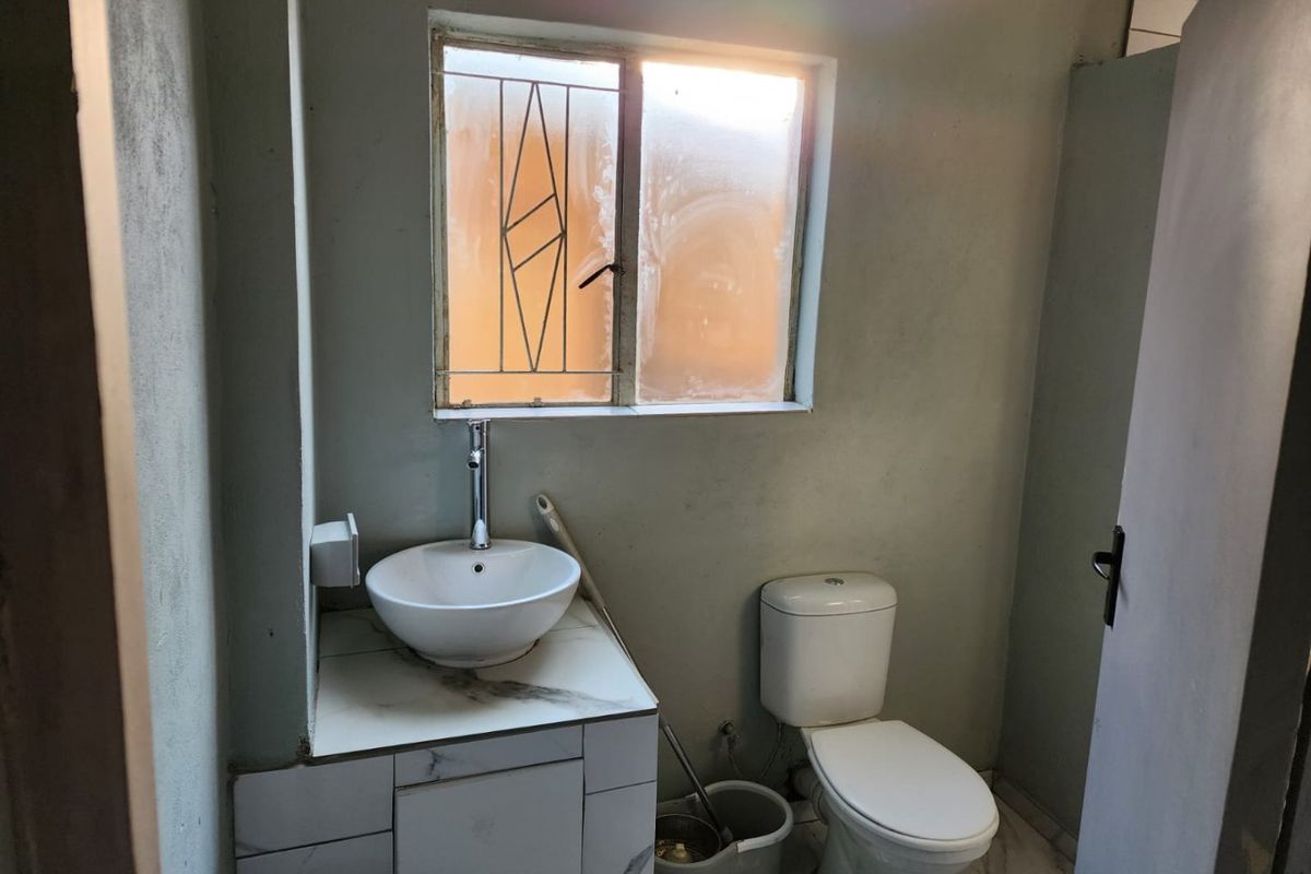 A compact bathroom featuring a modern vessel sink on a marble-look vanity, a standard toilet, and a window with security bars.