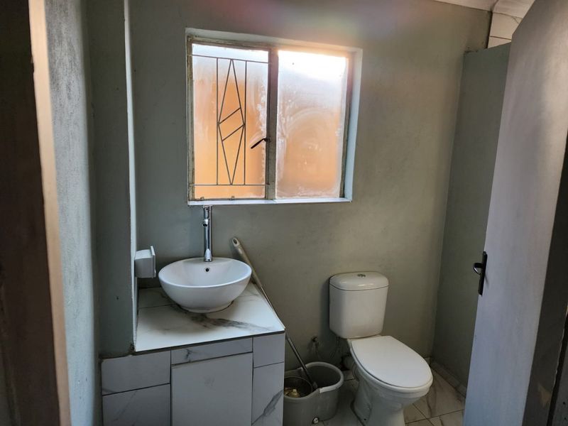 A compact bathroom featuring a modern vessel sink on a marble-look vanity, a standard toilet, and a window with security bars.