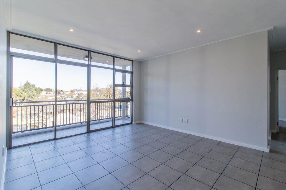 A bright and spacious open-plan living area featuring neutral tiled flooring, recessed lighting, and large sliding doors leading to a private balcony.