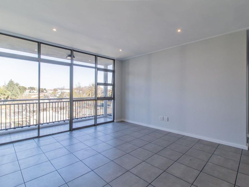 A bright and spacious open-plan living area featuring neutral tiled flooring, recessed lighting, and large sliding doors leading to a private balcony.
