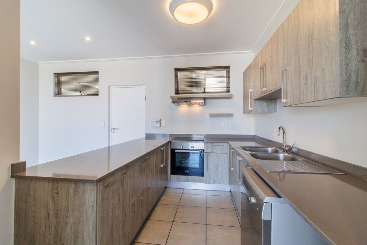 Modern kitchen featuring wood-finish cabinetry, stone countertops, integrated oven, extractor fan, and tiled flooring in a clean, well-lit space.
