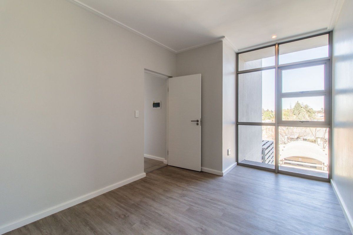 A bright and empty bedroom featuring modern laminate flooring and large floor-to-ceiling windows that provide ample natural light.