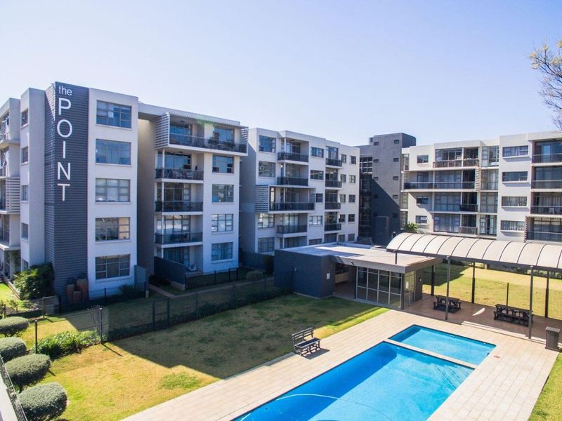 Aerial view of the apartment complex featuring a swimming pool, covered outdoor entertainment area, and landscaped garden spaces.