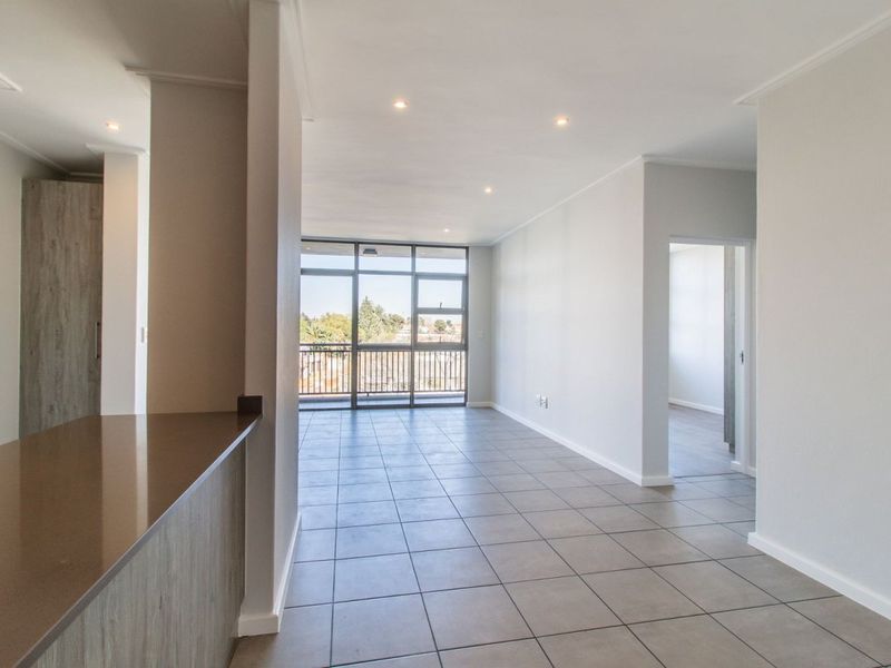 A bright and spacious open-plan living area featuring neutral tiled flooring, recessed lighting, and direct access to a balcony through large glass doors.