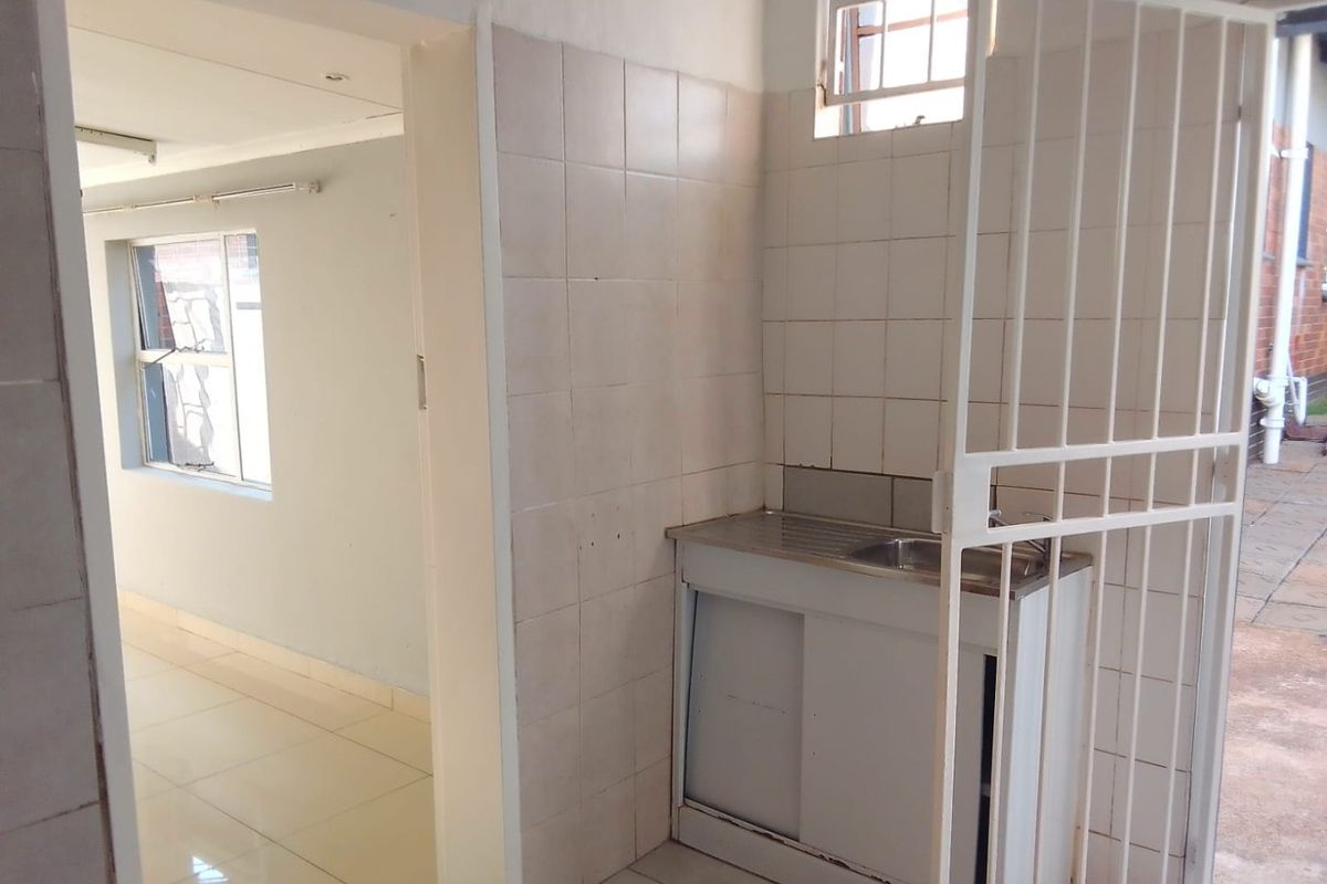 A functional scullery area featuring a stainless steel sink, tiled splashback, and direct access to the adjacent living space.