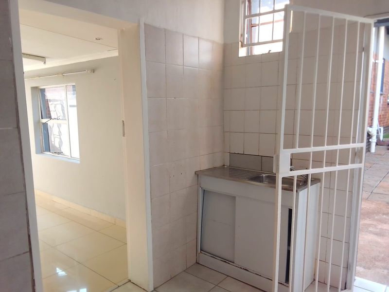 A functional scullery area featuring a stainless steel sink, tiled splashback, and direct access to the adjacent living space.