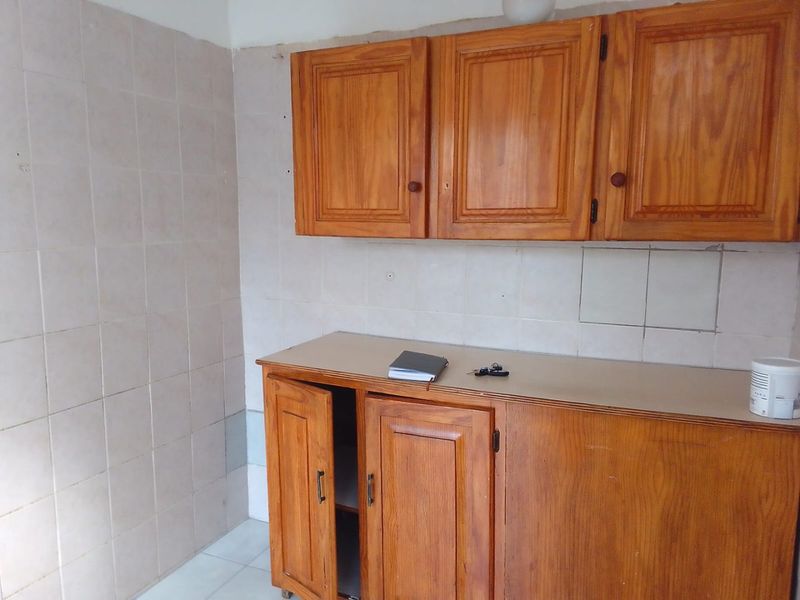A dated kitchen area featuring wooden cabinetry, tiled splashbacks, and tiled flooring, offering a blank canvas for potential modernization and renovation.