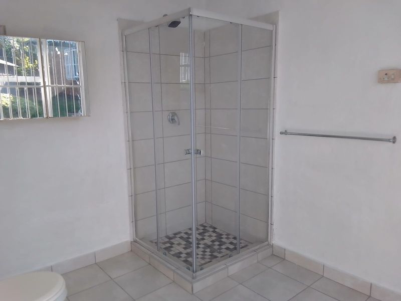 A clean, functional bathroom featuring a corner shower enclosure with tiled walls and flooring, complemented by a wall-mounted towel rail.
