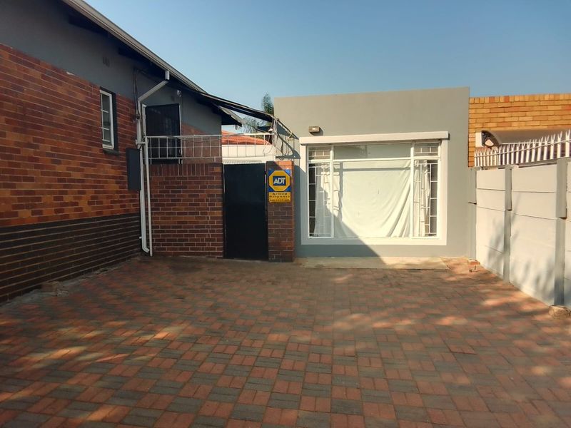 A paved rear courtyard area featuring brick walling, a secure gate, and a modern grey-rendered extension with large windows.